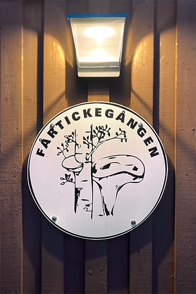 Fårtickegårdens Logotyp uppsatt på träpanelvägg och belyst med lykta